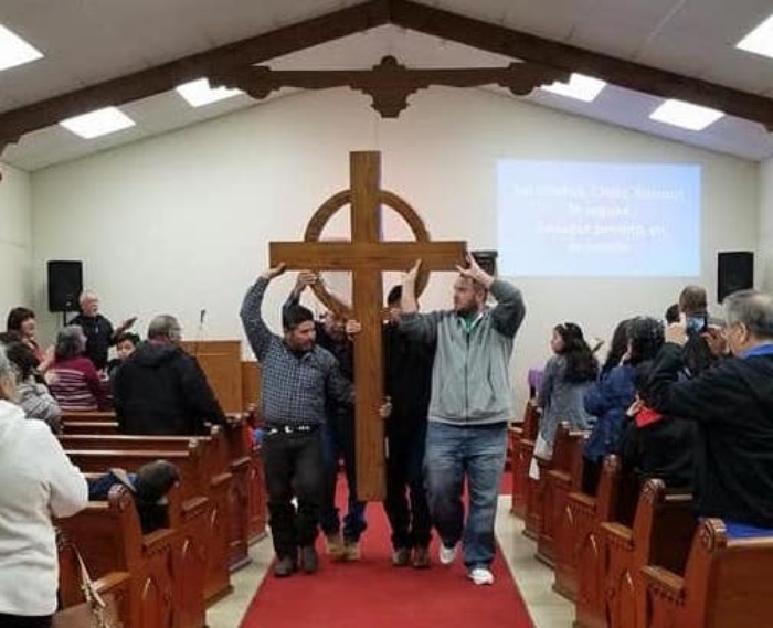 Men carrying a wooden cross down the aisle of a church