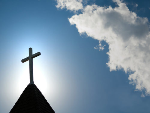 A wood cross on an old church steeple backlighted by a rising sun. Some copy space.