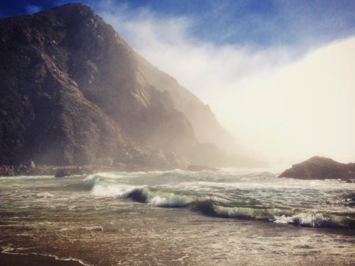 Waves crashing on the sand with mountains in the back
